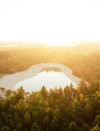 Luchtfoto van een meer omgeven door bos bij zonsondergang in vakantiepark De Kremmer, Drenthe, Nederland.
