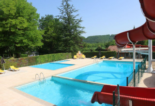 Swimmingpool med rutsjebane og liggestole på Camping Le Céou i Nouvelle-Aquitaine, Frankrig, omgivet af træer.