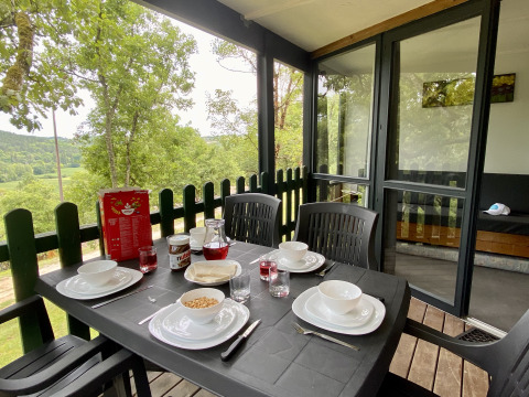 Outdoor breakfast table set for four on a glamping terrace overlooking forest and countryside.