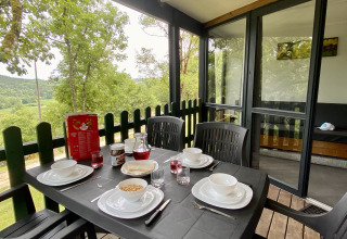 Outdoor breakfast table set for four on a glamping terrace overlooking forest and countryside.