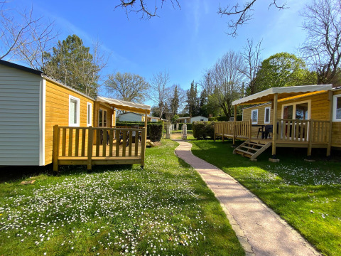 Holiday cabins at Camping Le Céou in Nouvelle-Aquitaine, France, surrounded by green grass and flowers.