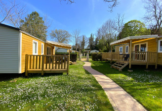 Holiday cabins at Camping Le Céou in Nouvelle-Aquitaine, France, surrounded by green grass and flowers.