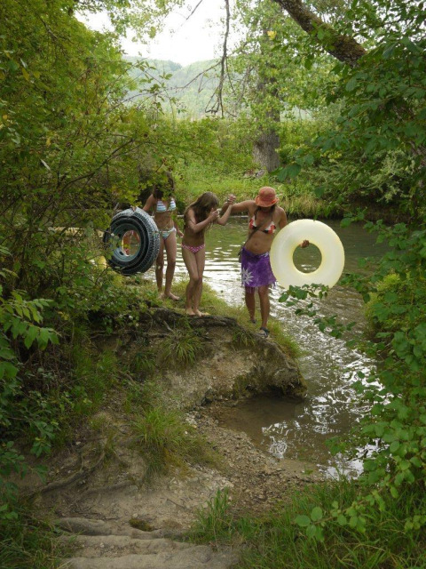 Children in swimsuits with inner tubes heading to a river at Camping Le Céou in Nouvelle-Aquitaine, France.
