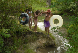 Children in swimsuits with inner tubes heading to a river at Camping Le Céou in Nouvelle-Aquitaine, France.