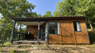 Cabane en bois de glamping avec terrasse couverte et salon extérieur, entourée d’arbres verdoyants.