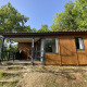 Wooden glamping cabin with a covered porch and outdoor seating, surrounded by lush green trees.