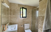 Salle de bain moderne avec carrelage beige, fenêtre, douche, toilette et lavabo dans un glamping.