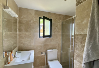 Moderne badkamer met beige tegels, raam, douche, toilet en lavabo in een glamping accommodatie.