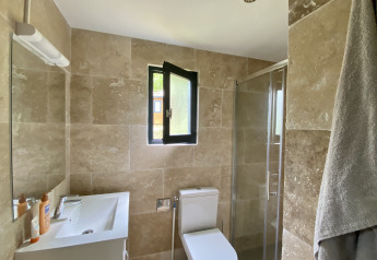 Bagno moderno con piastrelle beige, finestra, doccia, WC e lavandino in un alloggio glamping.