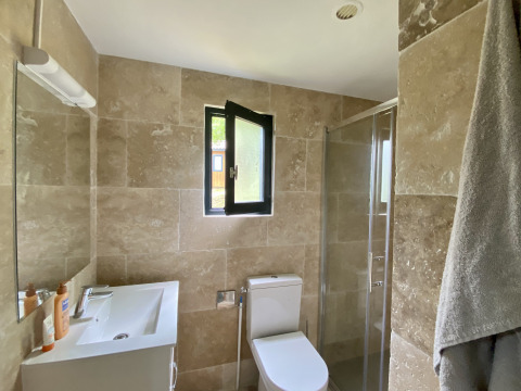 Moderne badkamer met beige tegels, raam, douche, toilet en lavabo in een glamping accommodatie.