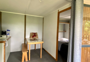 Innenraum einer Glamping-Unterkunft mit Tisch, Bank, Küchenzeile und Blick ins Schlafzimmer.