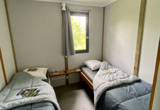 Glamping room with two single beds, grey bedding, a central window, and magazines placed on the duvets.