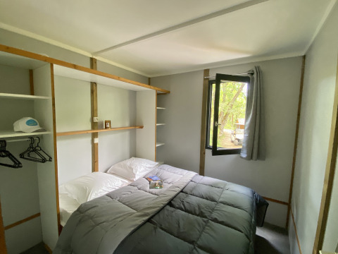 Hyggeligt glampingværelse med dobbeltseng, åbent vindue, opbevaring og udsigt til naturen.