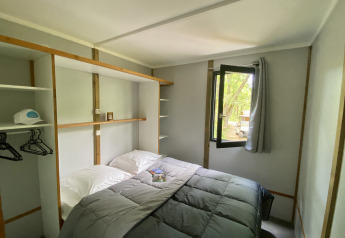 Acogedora habitación de glamping con cama doble, ventana abierta, estantes y vistas a la naturaleza.