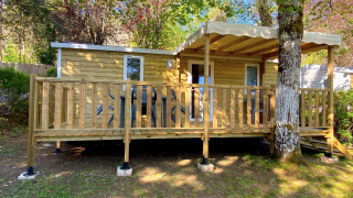 Cabaña Stacaravan de madera con terraza cubierta, rodeada de árboles y zona para sentarse afuera.