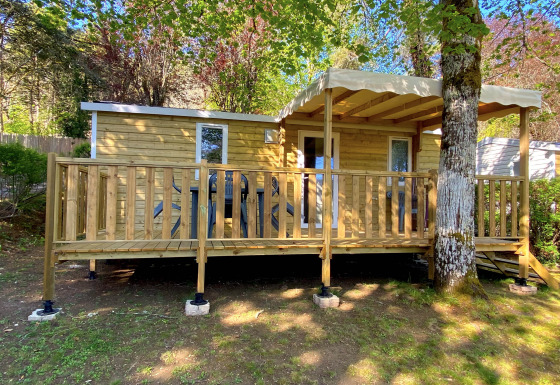 Stacaravan houten chalet met overdekt terras, gelegen tussen bomen en voorzien van zitplaatsen buiten.