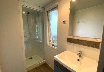 Modern bathroom in Stacaravan at Camping Le Céou, France, featuring shower, sink, mirror, and open window.