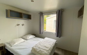 Camera luminosa con letto matrimoniale e finestra in una Stacaravan presso Camping Le Céou, Francia.