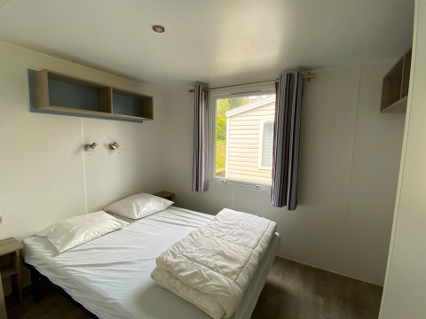 Lichte slaapkamer met tweepersoonsbed en raam in een Stacaravan op Camping Le Céou, Frankrijk.