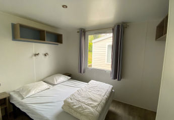 Helles Schlafzimmer mit Doppelbett und Fenster in einer Stacaravan-Unterkunft auf Camping Le Céou, Frankreich.
