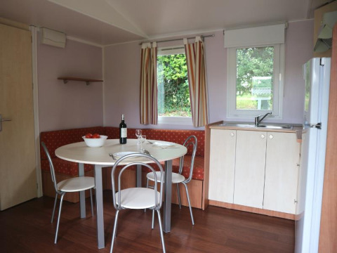 Dining area and kitchenette in Stacaravan met airco at Camping Le Céou, France, with round table and corner bench.