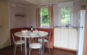 Dining area and kitchenette in Stacaravan met airco at Camping Le Céou, France, with round table and corner bench.