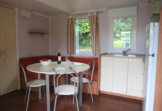 Dining area and kitchenette in Stacaravan met airco at Camping Le Céou, France, with round table and corner bench.