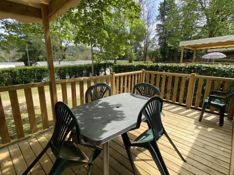 Wooden deck with plastic chairs and table at Stacaravan met airco at Camping Le Céou, surrounded by greenery.