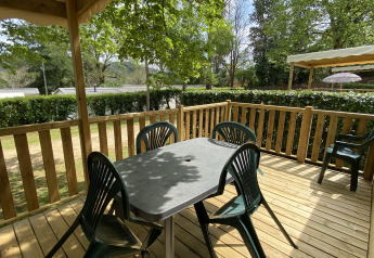 Houten terras met plastieken stoelen en tafel bij Stacaravan met airco op Camping Le Céou, tussen het groen.