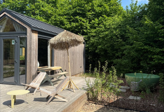 Terraza soleada en Tiny Home MET DUTCHTUB - GENT con tumbonas, sombrilla y tina verde al aire libre.