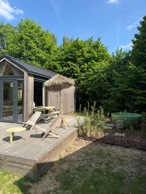 Udendørs terrasse ved Tiny Home MET DUTCHTUB - GENT med liggestole, parasol og grøn badetønde.