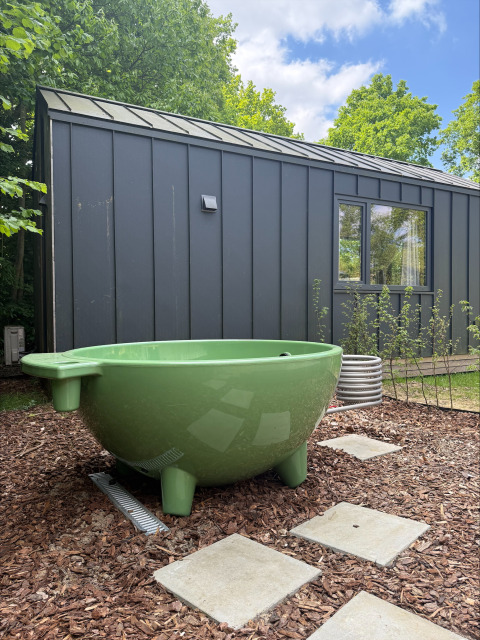 Tina verde al aire libre frente a una tiny house negra en Tiny Home MET DUTCHTUB - GENT, Urban-Gardens, Bélgica.