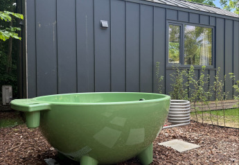 Tina verde al aire libre frente a una tiny house negra en Tiny Home MET DUTCHTUB - GENT, Urban-Gardens, Bélgica.