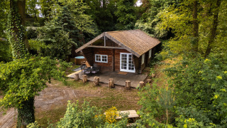 Sfeervolle houten lodge 'Huys van de Boswachter' met bubbelbad, omgeven door een groene bosrijke omgeving.