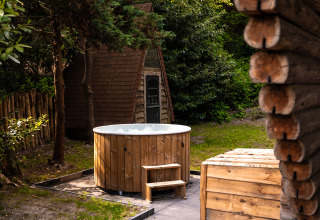Outdoor wooden hot tub at Huys van de Boswachter lodge in Sandberghe, Netherlands, surrounded by trees.