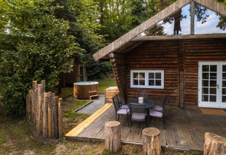 Outdoor view of 'Huys van de Boswachter' lodge with a wooden deck, seating area and hot tub at Sandberghe.