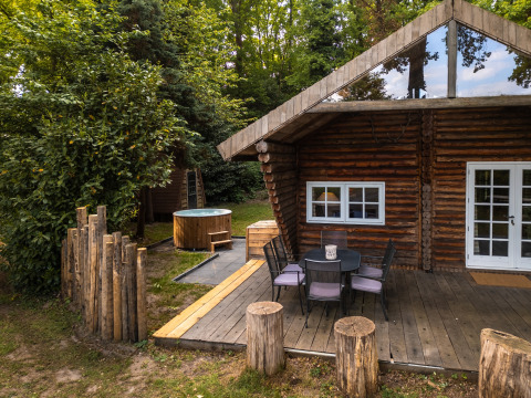 Buitenbeeld van 'Huys van de Boswachter' lodge met houten terras, zitje en bubbelbad bij Sandberghe.