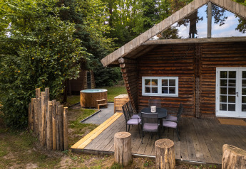 Vista exterior del lodge 'Huys van de Boswachter' con terraza de madera, mesa y jacuzzi en Sandberghe.
