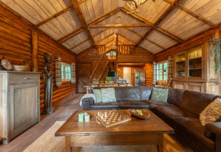 Sala de estar acogedora de madera en la cabaña 'Huys van de Boswachter' en Sandberghe, Países Bajos, con sofá grande.