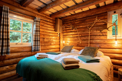 Knusse houten lodge slaapkamer met tweepersoonsbed, groene dekens en warme verlichting in Sandberghe.