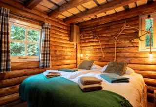 Knusse houten lodge slaapkamer met tweepersoonsbed, groene dekens en warme verlichting in Sandberghe.