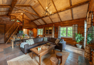 Cozy log cabin living room with vaulted ceiling, sectional sofa, and dining area at Sandberghe, Netherlands.