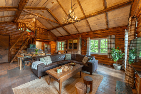 Acogedora sala de estar de cabaña de troncos con techo alto, sofá esquinero y comedor en Sandberghe, Países Bajos.