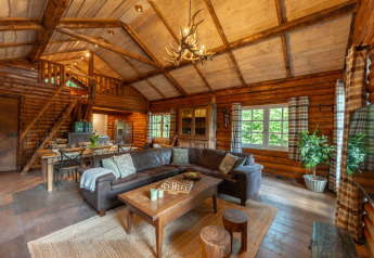 Acogedora sala de estar de cabaña de troncos con techo alto, sofá esquinero y comedor en Sandberghe, Países Bajos.