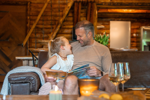 Padre e figlia leggono e ridono insieme in un'accogliente baita di Huys van de Boswachter, Sandberghe, Olanda.