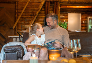 Padre e figlia leggono e ridono insieme in un'accogliente baita di Huys van de Boswachter, Sandberghe, Olanda.