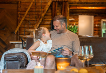 Vader en dochter lezen en lachen samen in een knusse blokhut bij Huys van de Boswachter, Sandberghe, Nederland.