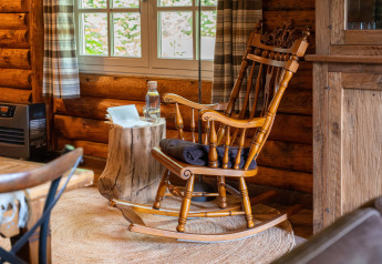 Traditionele houten schommelstoel bij het raam in een gezellige blokhut bij 'Huys van de Boswachter', Sandberghe.