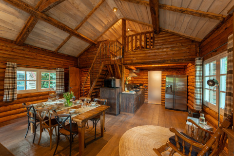 Interno accogliente di un lodge in legno a Huys van de Boswachter con tavolo da pranzo, cucina e soppalco.