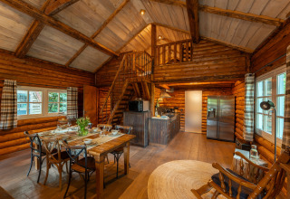 Knusse blokhut bij Huys van de Boswachter, met eetgedeelte, keuken, trap naar de mezzanine en houten interieur.